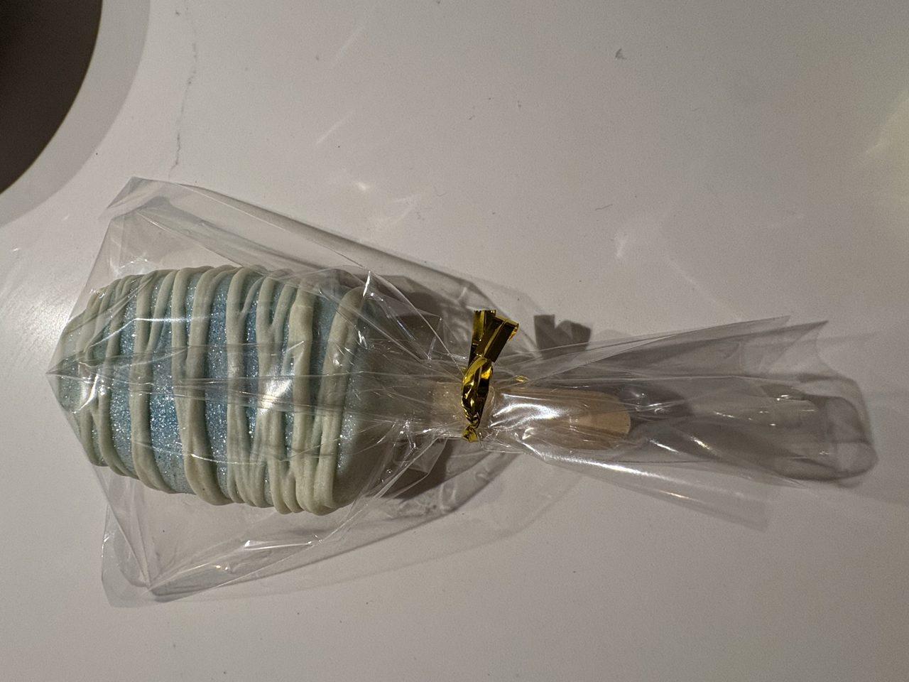 A wrapped pale blue cake pop with white drizzle
